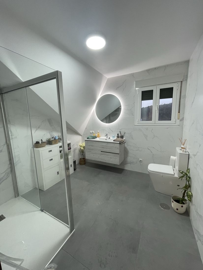 Bathroom with marble-look walls, grey large-format floor, backlit round mirror and floating vanity