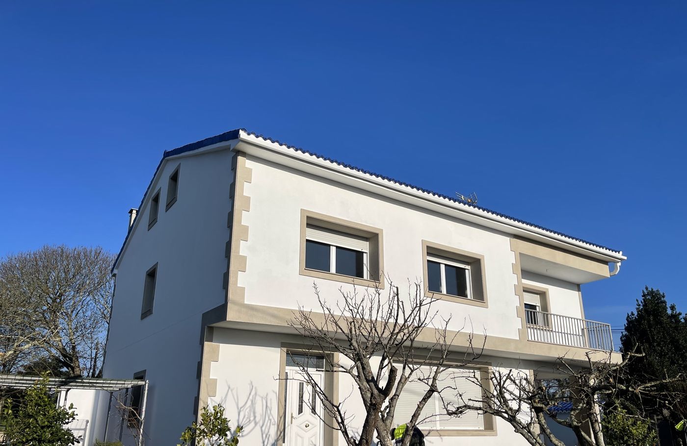 Front of renovated house with white facade, stone-look window surrounds and balcony
