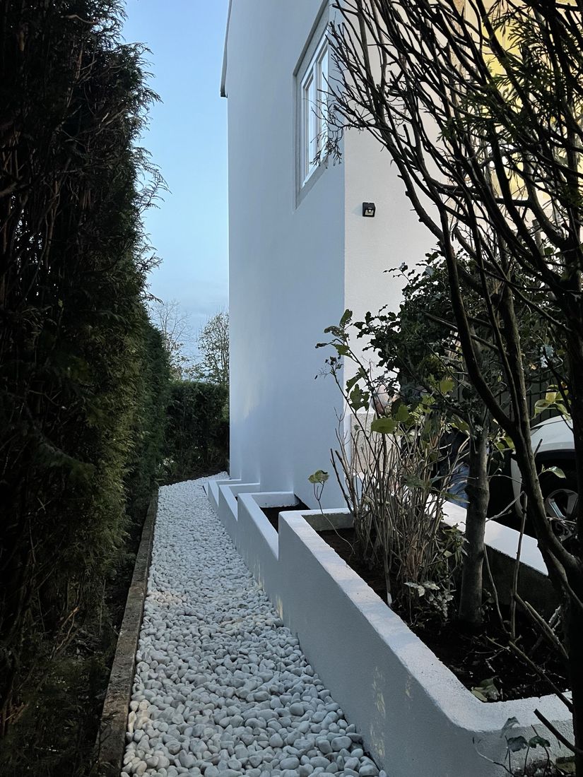 Side path with white pebbles and rendered planters along a freshly rendered wall