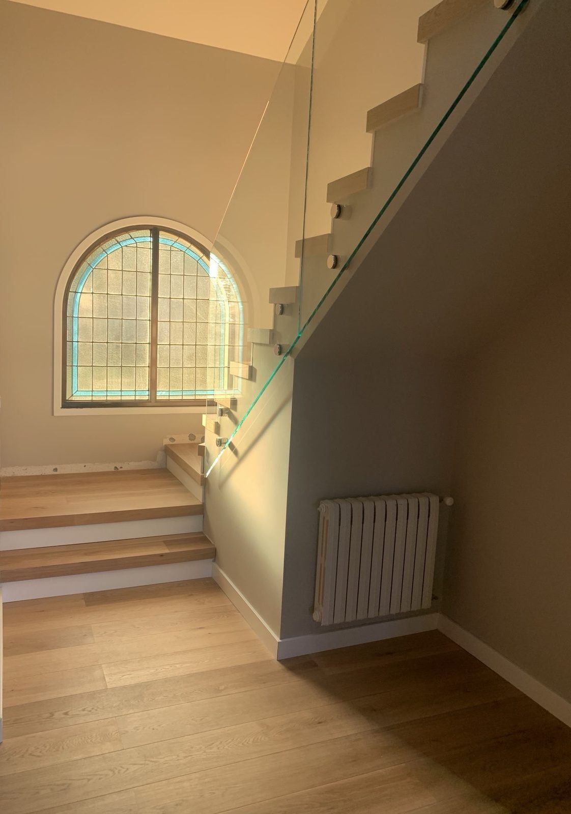 Staircase with oak treads, frameless glass railing and restored stained-glass arched window
