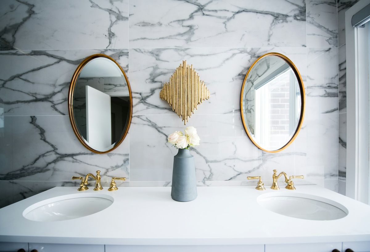 Double vanity bathroom with marble walls, round brass mirrors and brass fixtures