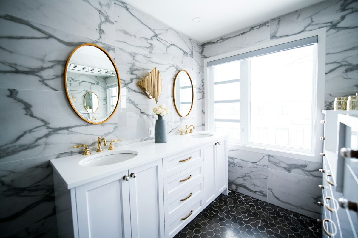 White vanity bathroom with marble walls and round brass mirrors
