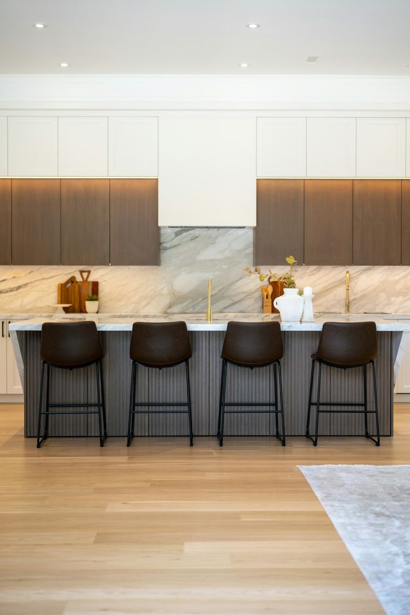 Kitchen with marble waterfall island, marble backsplash, walnut cabinetry and leather stools