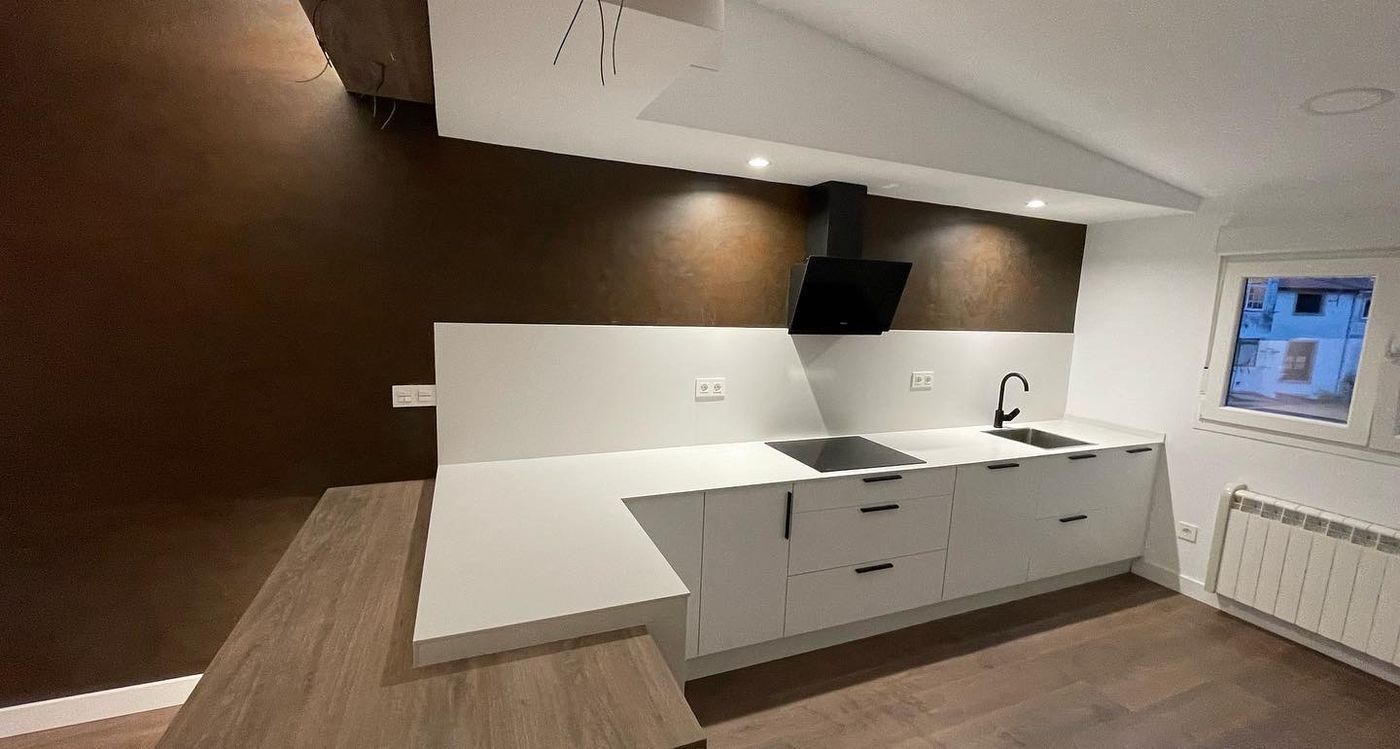 Wide view of white handleless kitchen against a bronze plaster feature wall