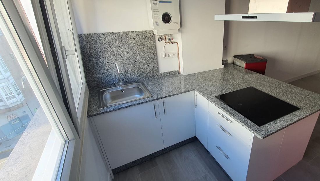 L-shaped kitchen with grey granite countertop and backsplash, white cabinets and induction cooktop