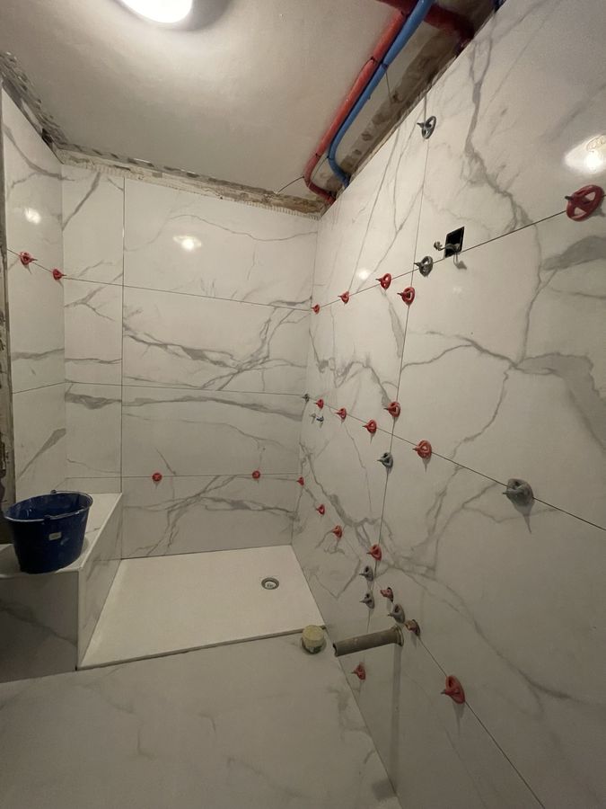 Marble-look large-format porcelain set with leveling clips in a shower