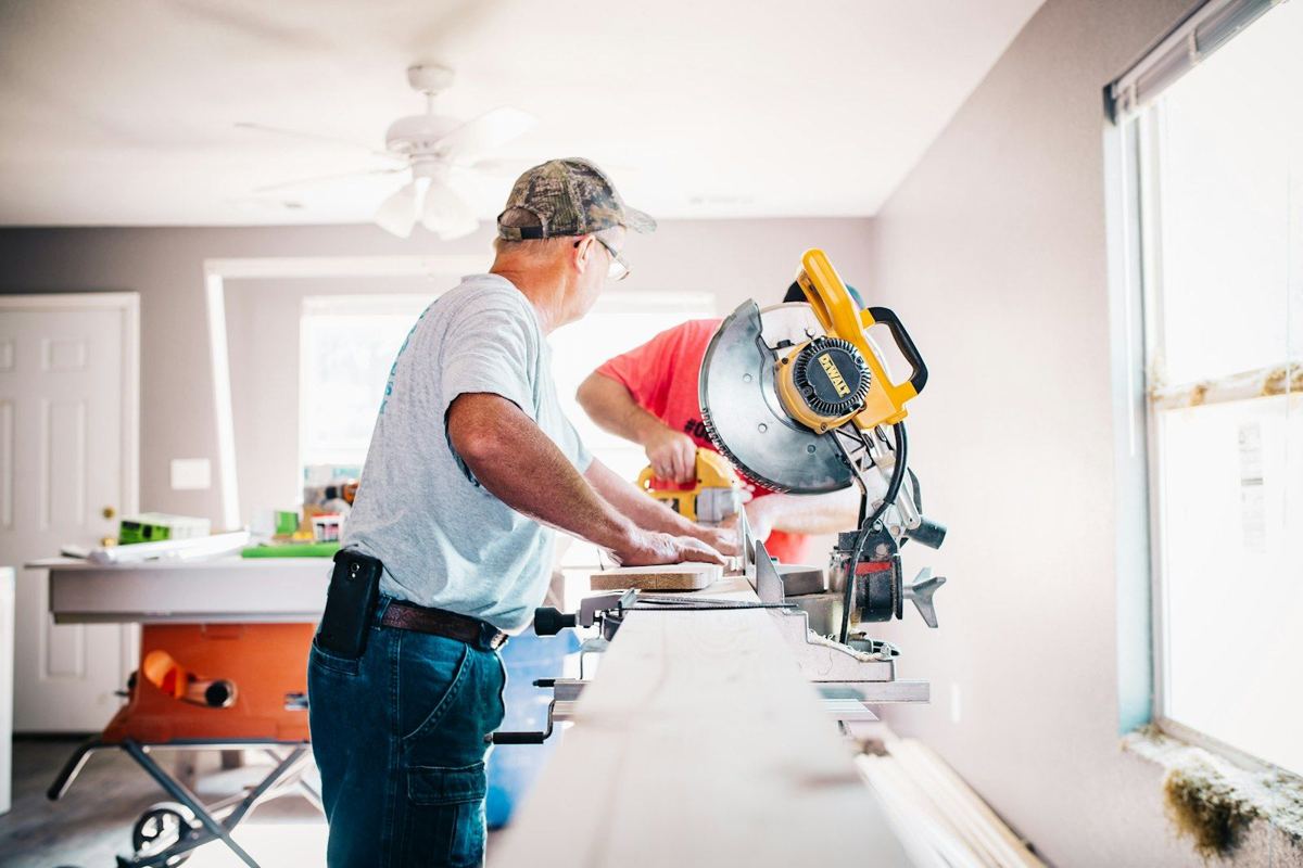 Carpenter cutting trim with a miter saw inside a home under renovation